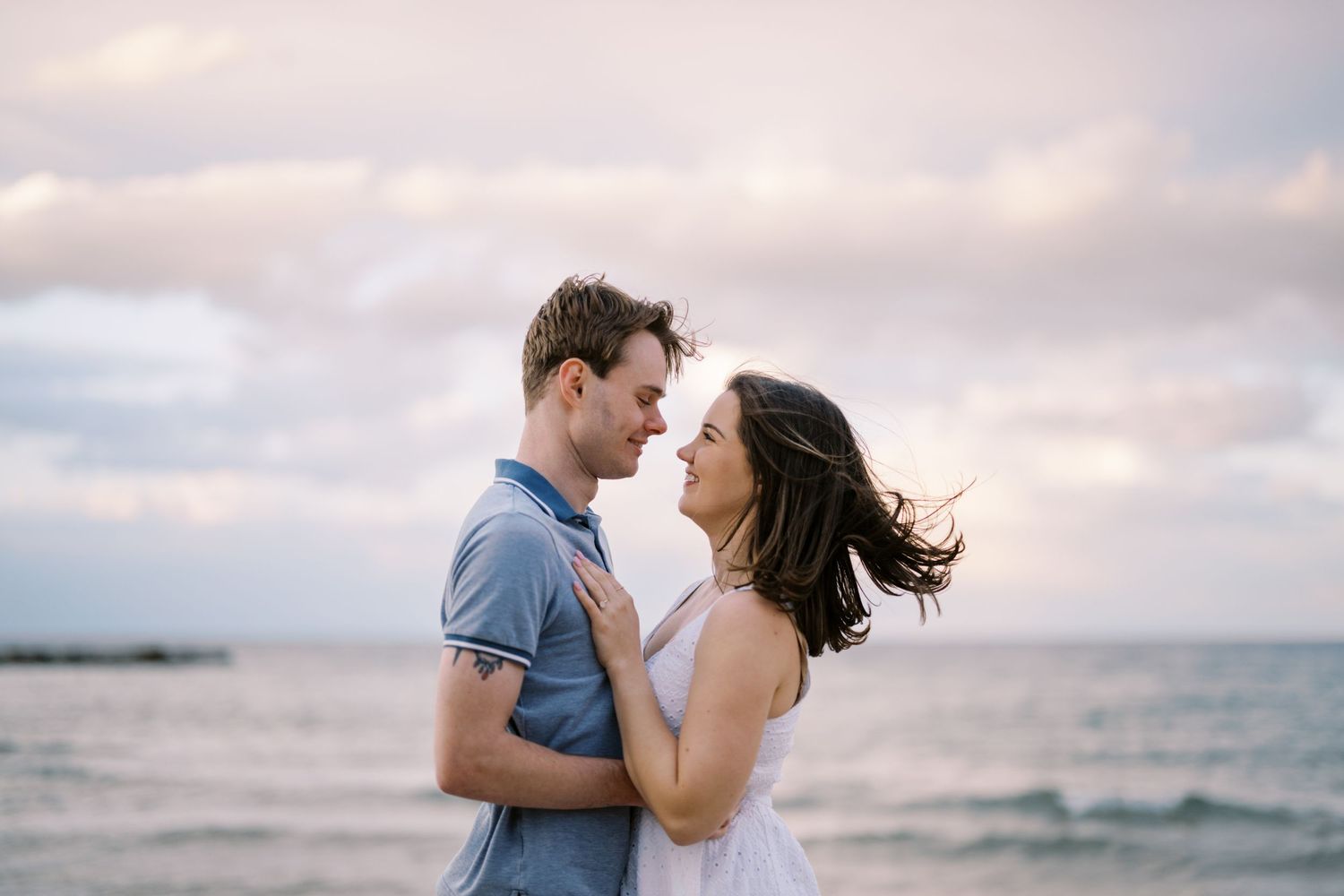 A romantic couple embraces on the beach during sunset with the ocean waves in the background.