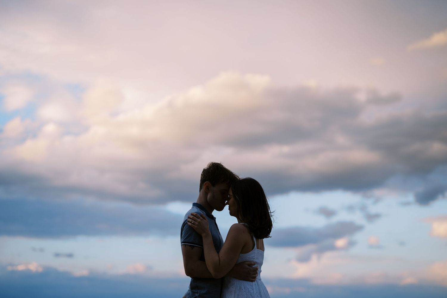 A silhouetted couple shares an intimate moment against a dramatic cloudy sky at dusk.