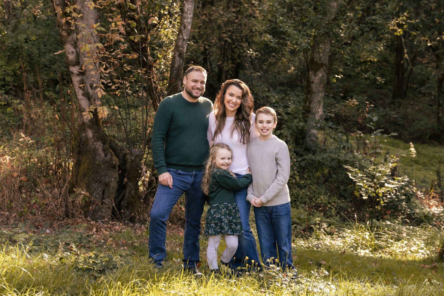 Casual outdoor family portrait in wooded setting during golden hour with trees and natural lighting.
