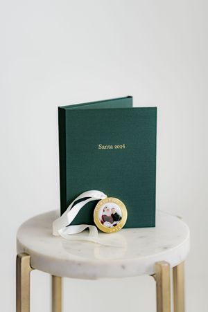 A green hardcover book titled 'Santa 2024' with a gold ornament on a marble and gold side table.
