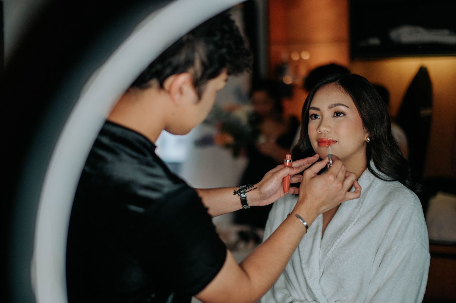 Makeup artist applying lipstick on bride during wedding preparation in front of ring light.