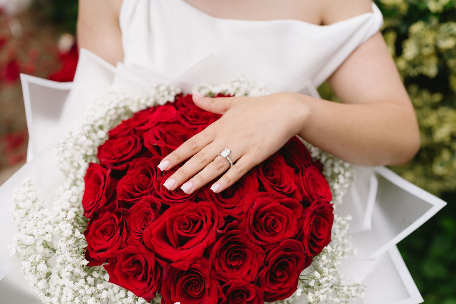 Close-up of engagement ring with bouquet of red roses and baby's breath flowers.