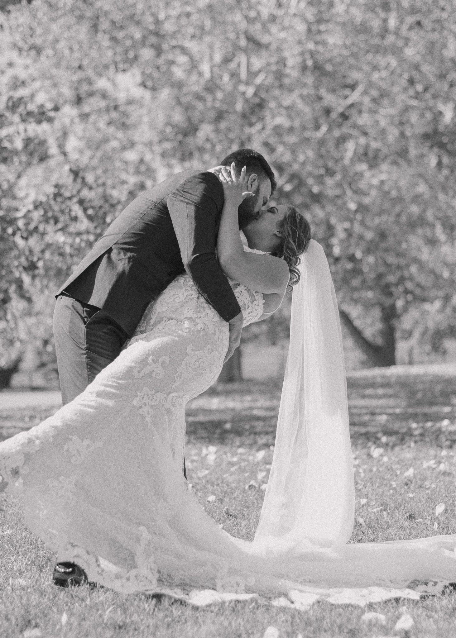 Black and white photo of bride and groom sharing a romantic kiss as he dips her, capturing classic essence.