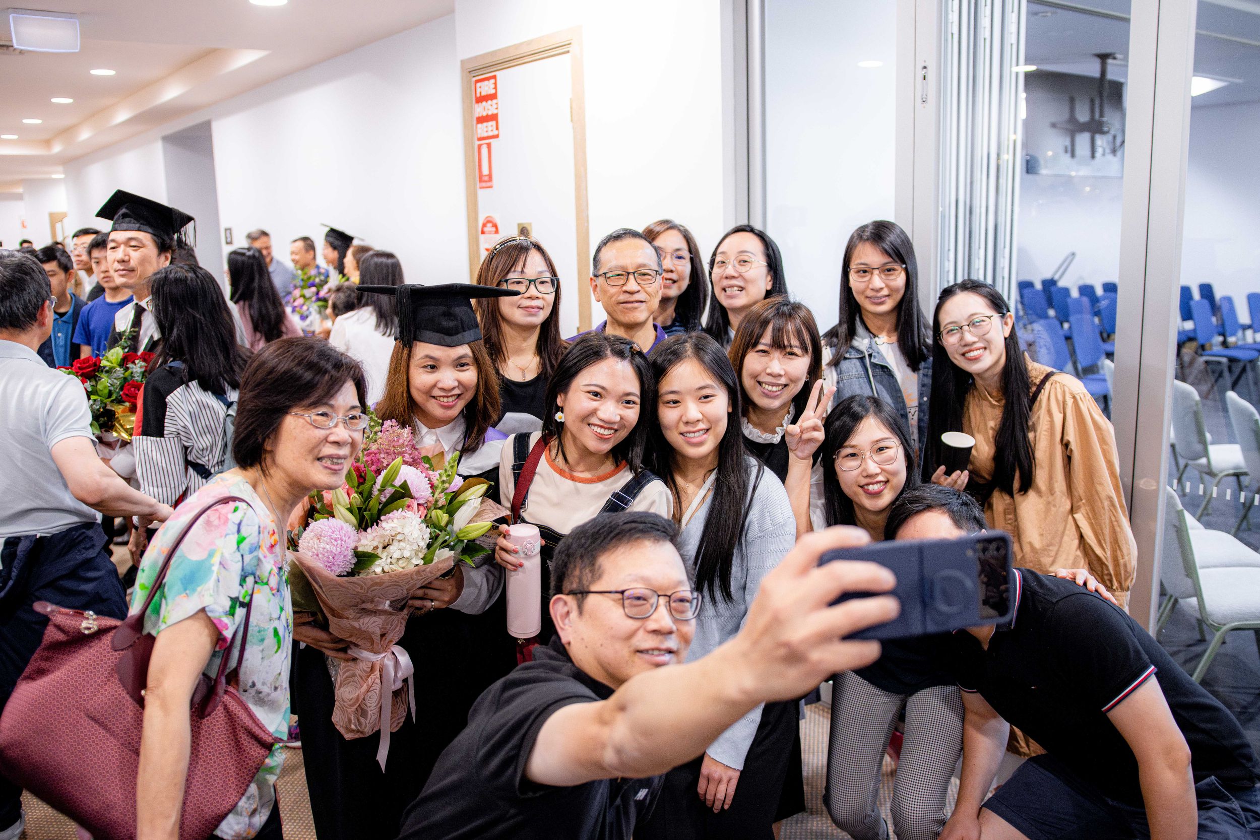 Group of graduates taking celebratory selfies in hallway after ceremony.