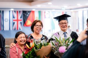 A graduation celebration with loved ones holding flower bouquets against a backdrop of international flags.