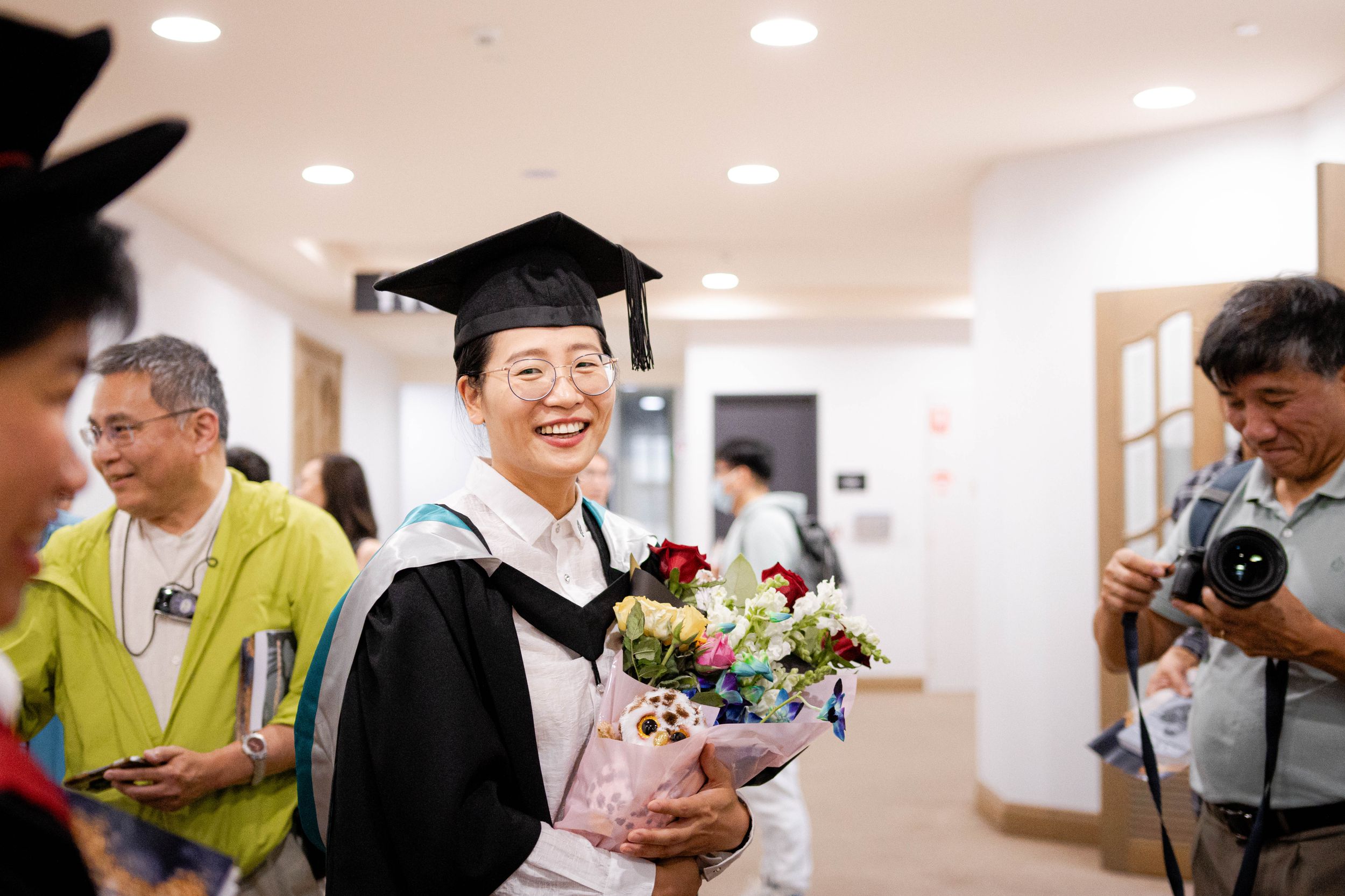 Graduate in cap and gown smiles while holding a floral bouquet during celebration ceremony.
