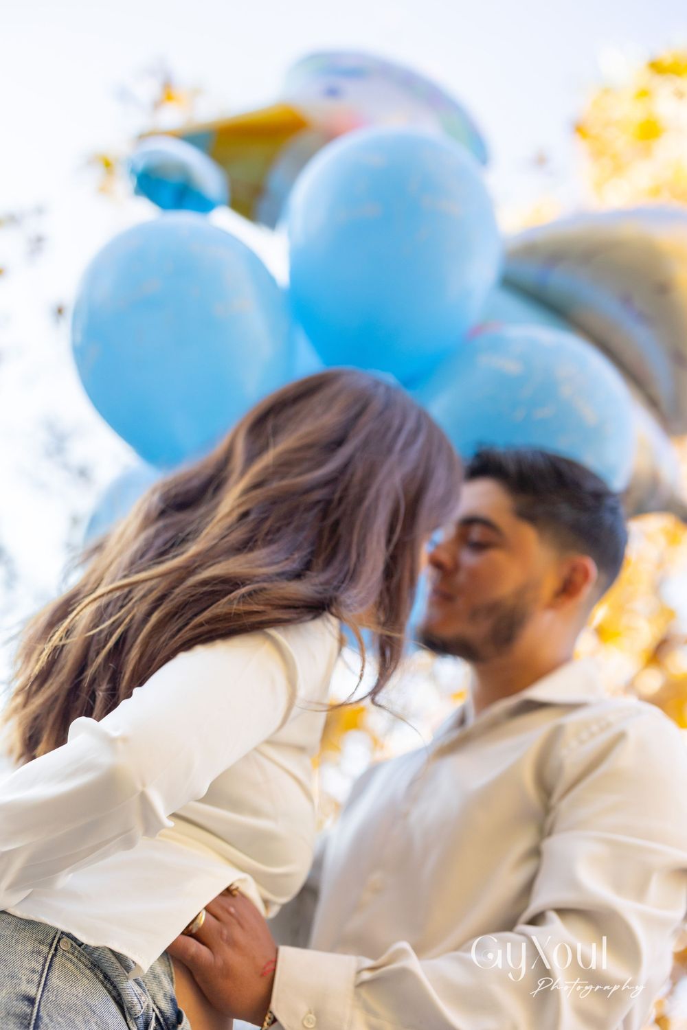 A romantic moment captured with blue balloons in the background during a pregnancy announcement.
