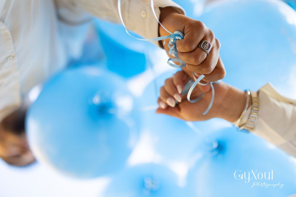 Close-up view of hands holding light blue balloons against a bright sky.