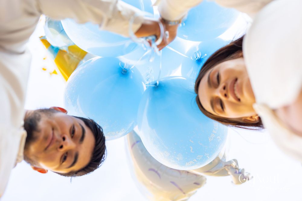 Looking up at a couple smiling while holding blue balloons outdoors.