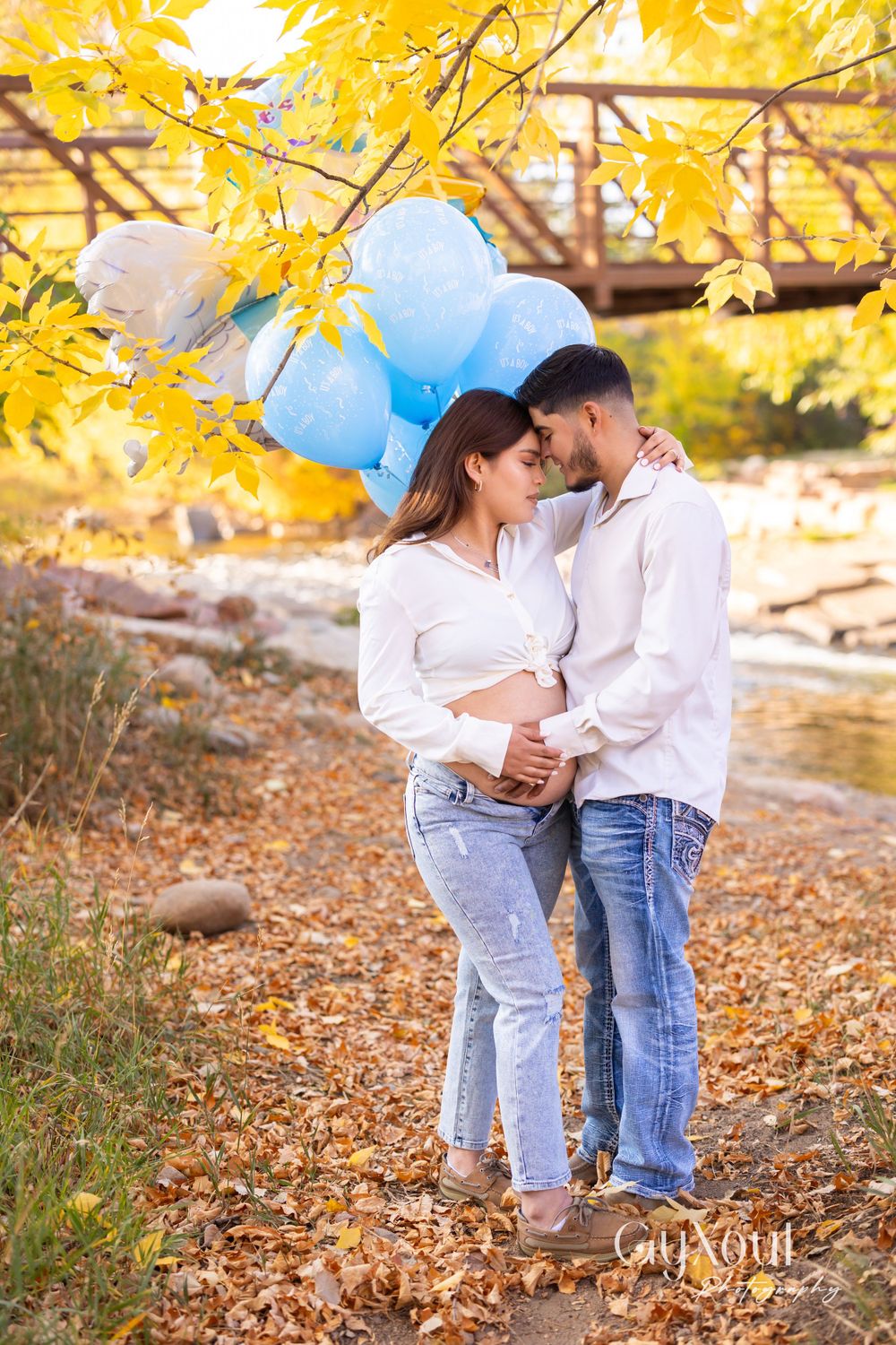 An intimate maternity portrait with blue balloons and fall foliage in the background.