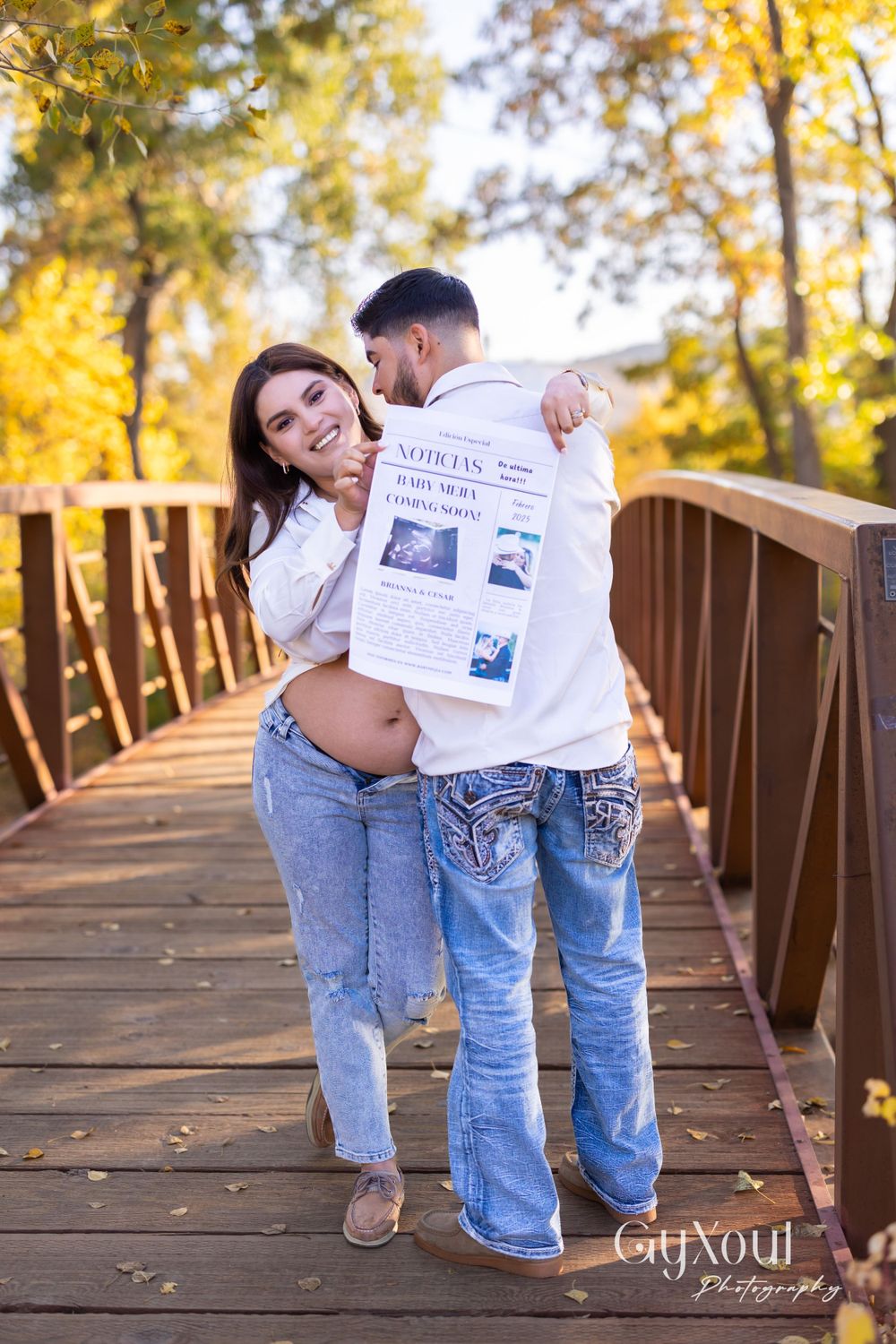 A playful pregnancy announcement photo on a wooden bridge with ultrasound images.