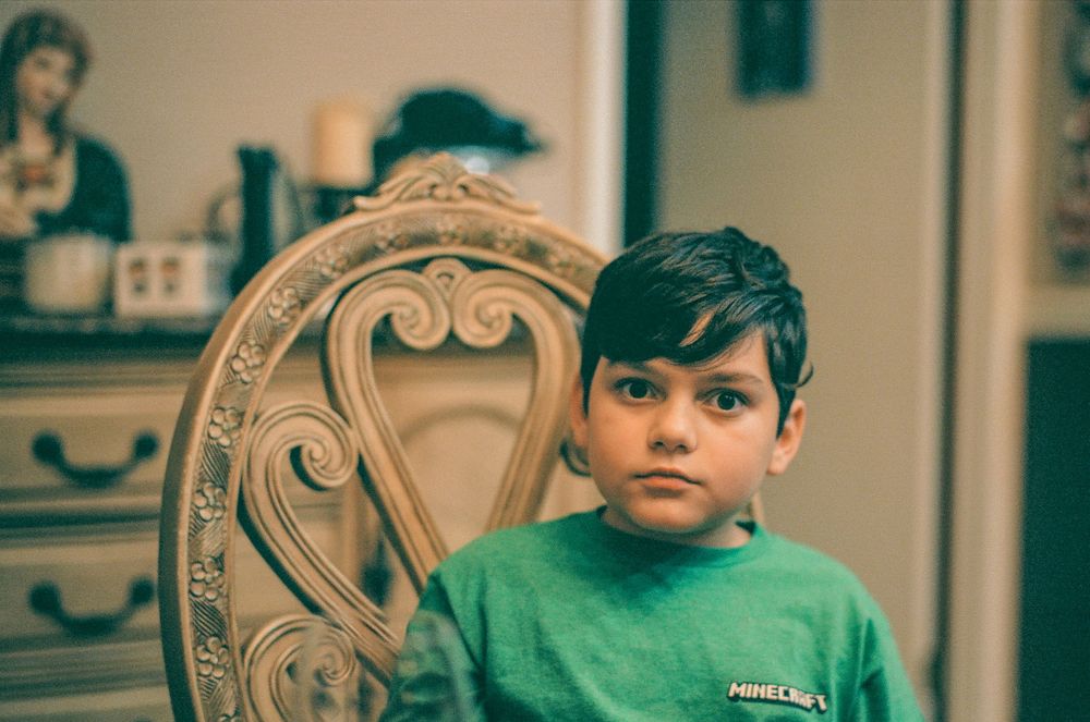 A young person sits in an ornate vintage chair indoors.