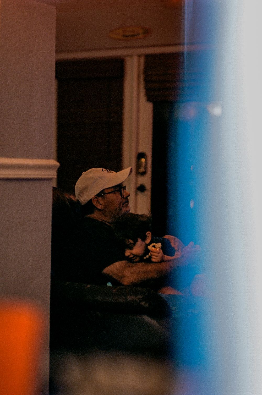 A person wearing a baseball cap sits in dim lighting indoors.