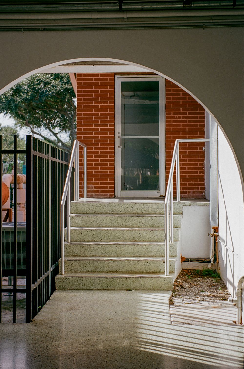 An arched entryway with brick accents and concrete steps leads to a glass door.