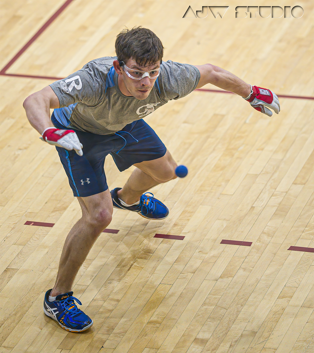 Handball player lunges to hit a small ball during an indoor handball match on wooden court.