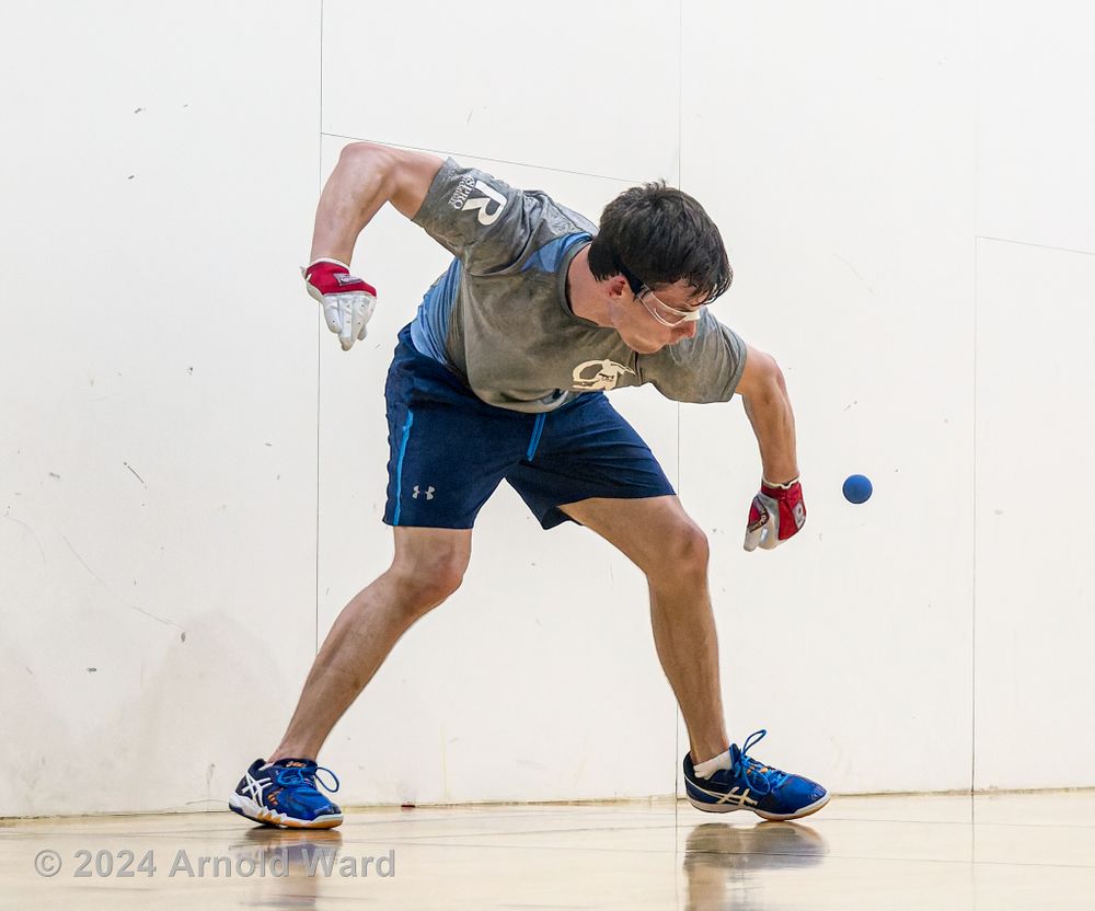 Handball player in blue shorts stretches to return a shot during indoor handball match.