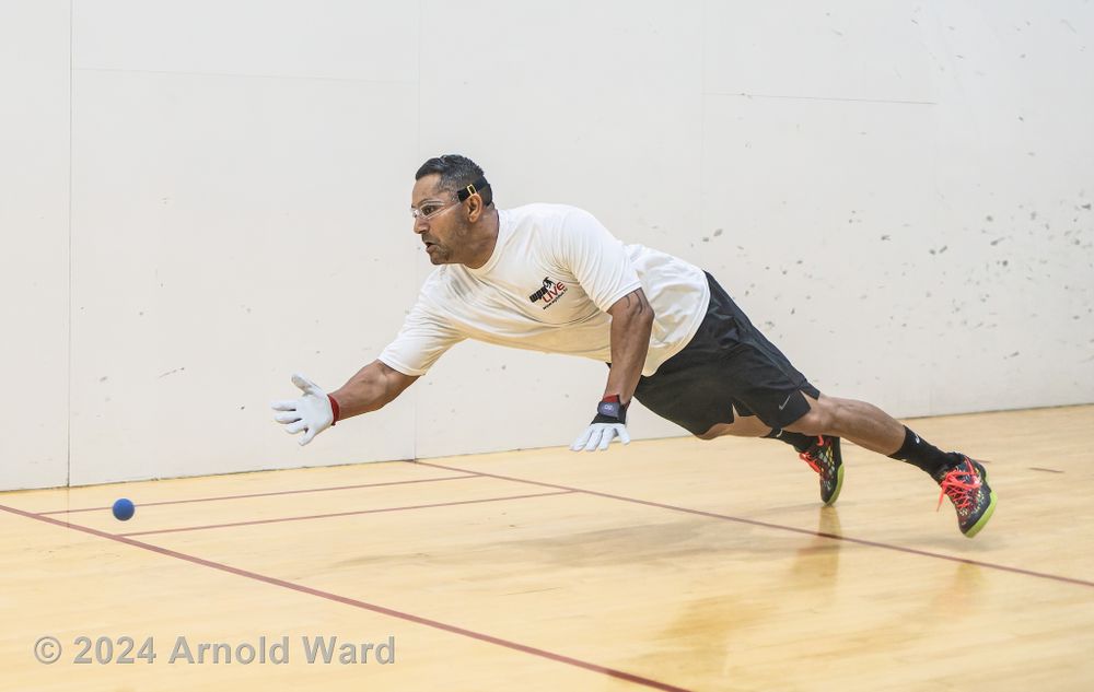 Player stretches into a full split position to return a low shot on indoor court.