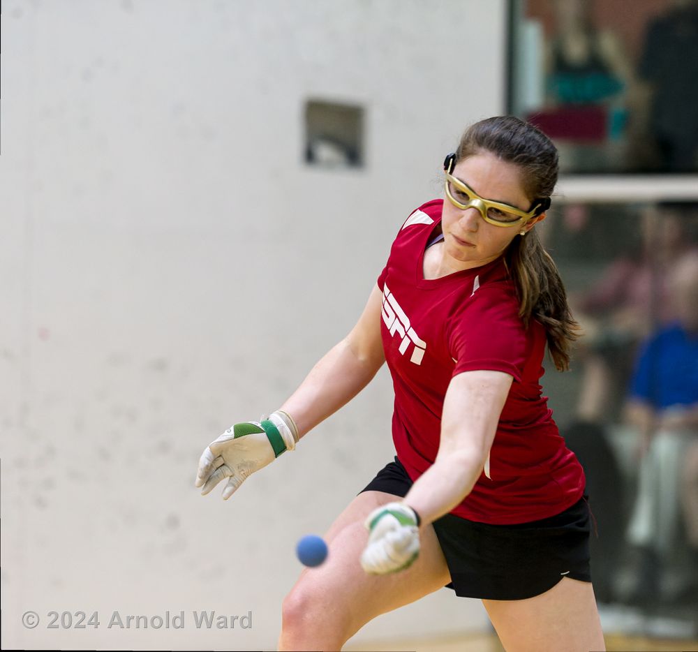 Handball player in red shirt focuses intently while preparing to return a shot.