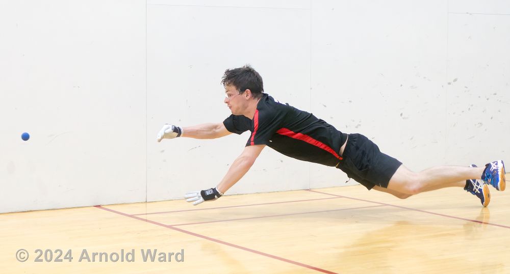 Handball player dives horizontally through the air to make an athletic shot on indoor court.