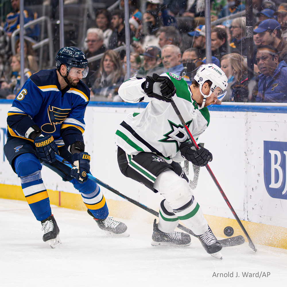 A St. Louis Blues hockey player battles against a Dallas Stars player along the boards during a game.