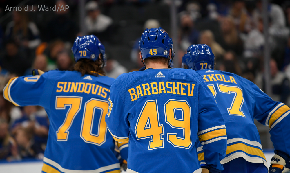 Three St. Louis Blues players wearing blue jerseys with yellow numbers celebrate together during a game.