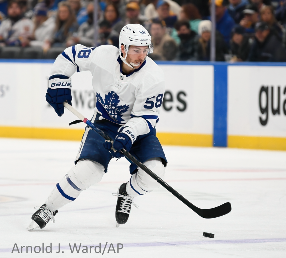 A player in a white Toronto Maple Leafs jersey skates with the puck during a hockey match.