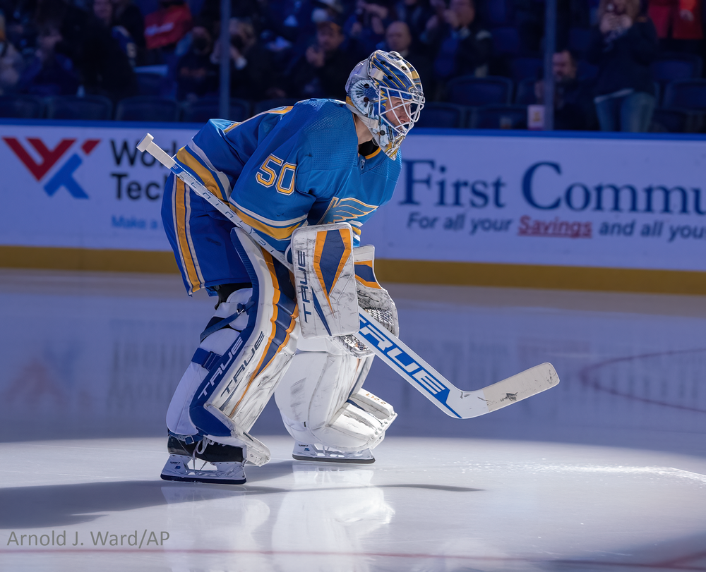 A t. Louis Blues goalie in a blue and yellow uniform stands ready in position during a hockey game.