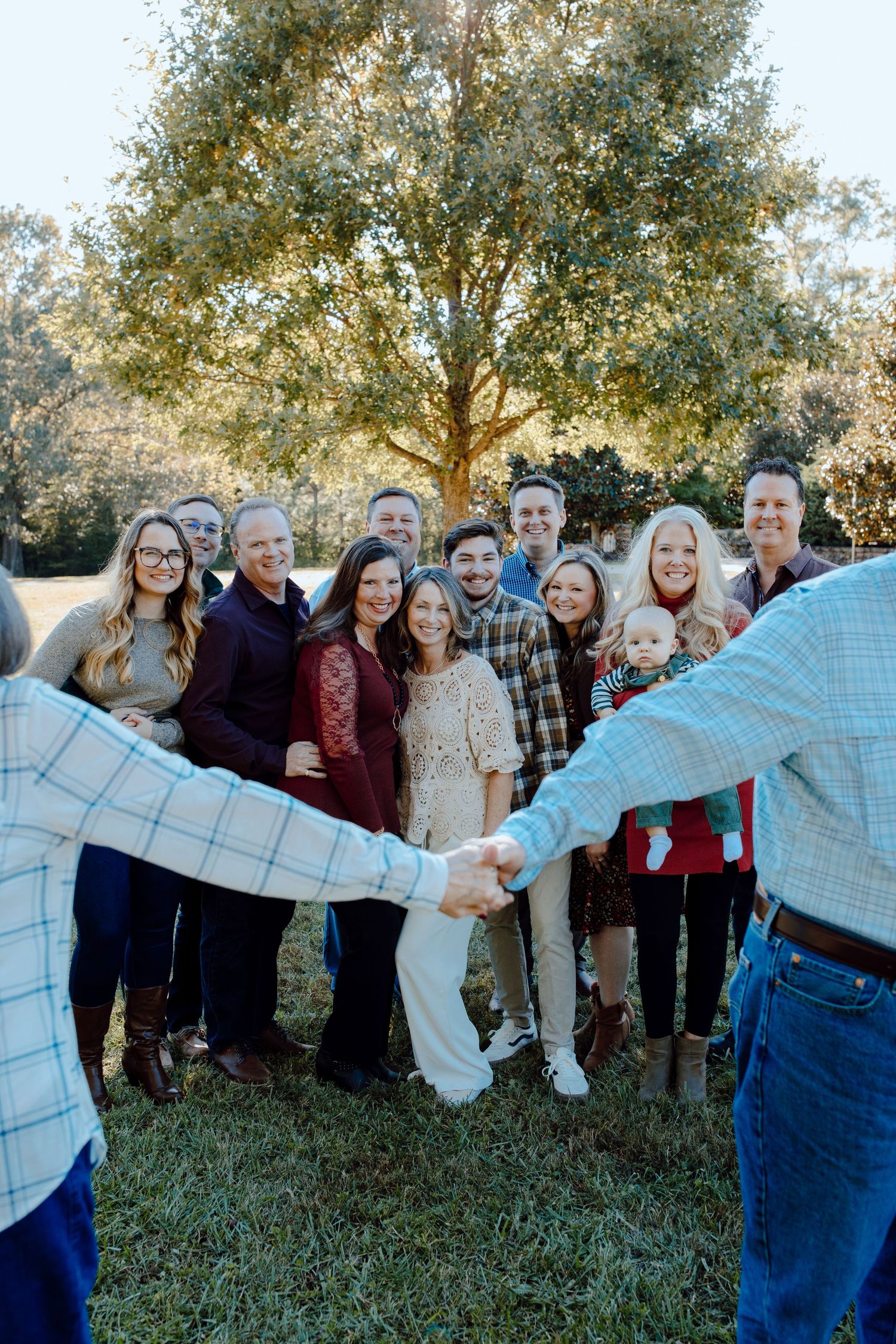 A large group poses together under a tree while two people shake hands in the foreground.