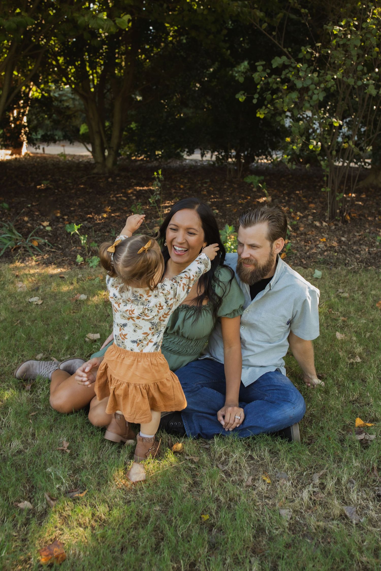 A joyful family shares a playful moment together on grass in dappled sunlight.