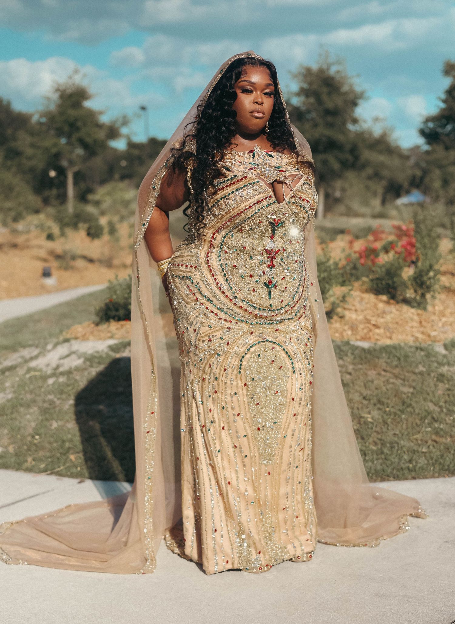Woman in stunning gold beaded gown with sheer cape posing outdoors.