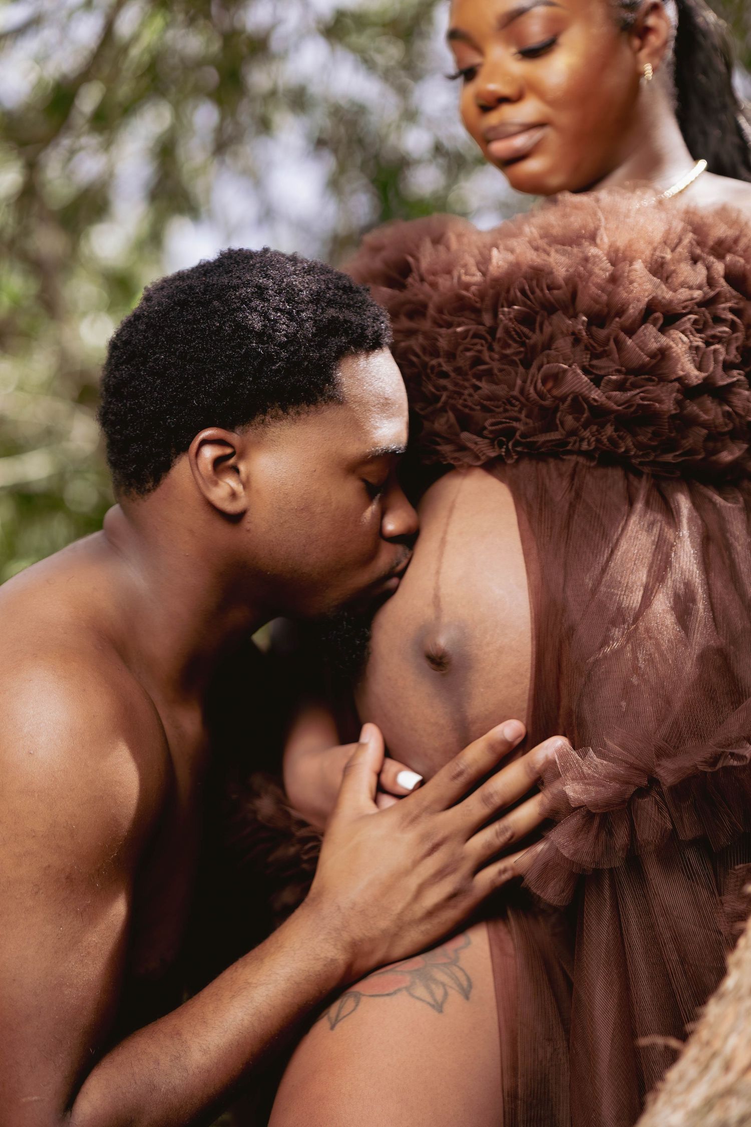 Intimate maternity photo of a man tenderly kissing a pregnant womans baby bump outdoors.