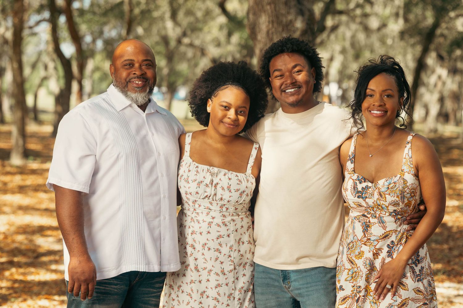 Happy family of four smiling together outdoors among trees.