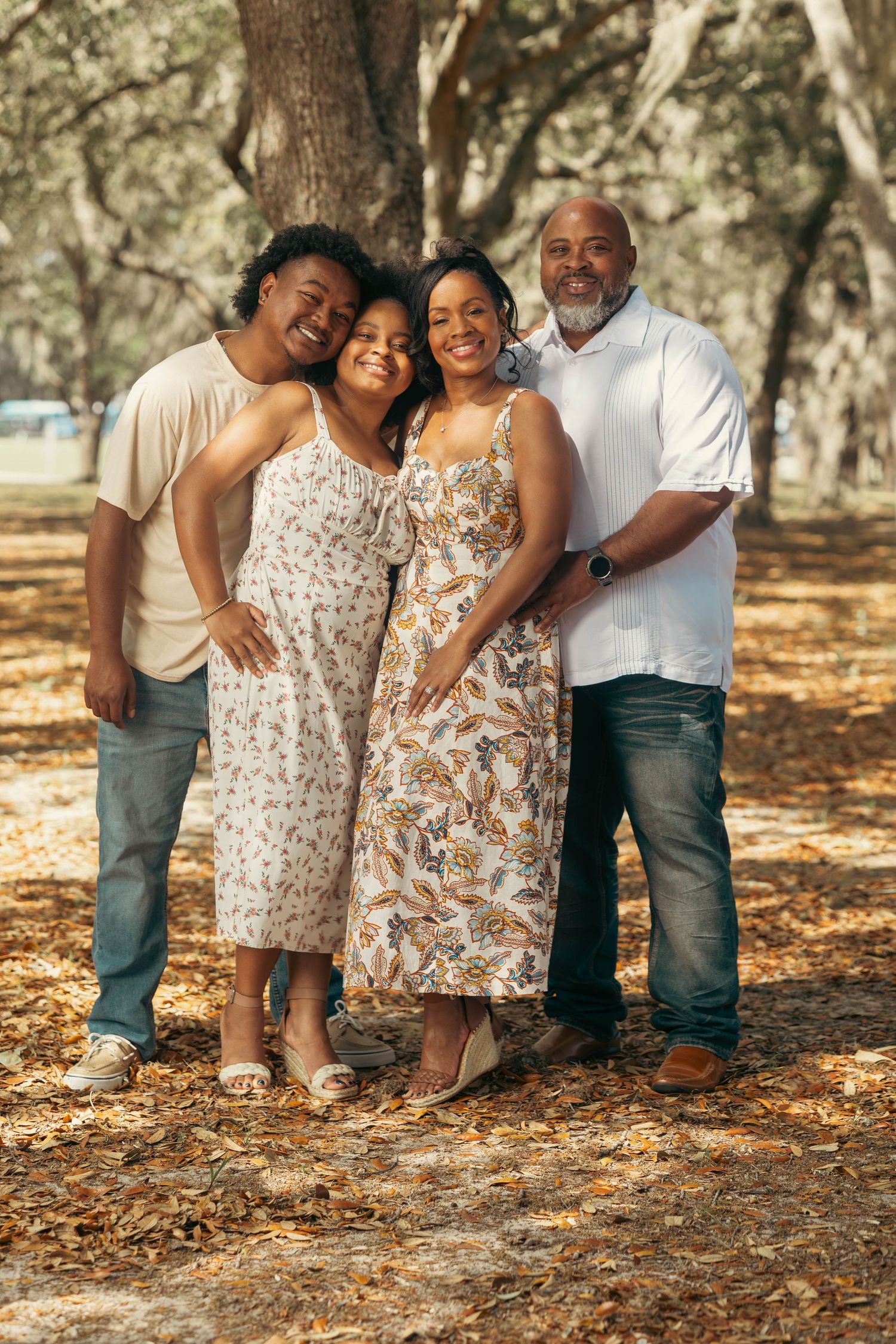 Family of four posing warmly together in a sunlit wooded park setting.
