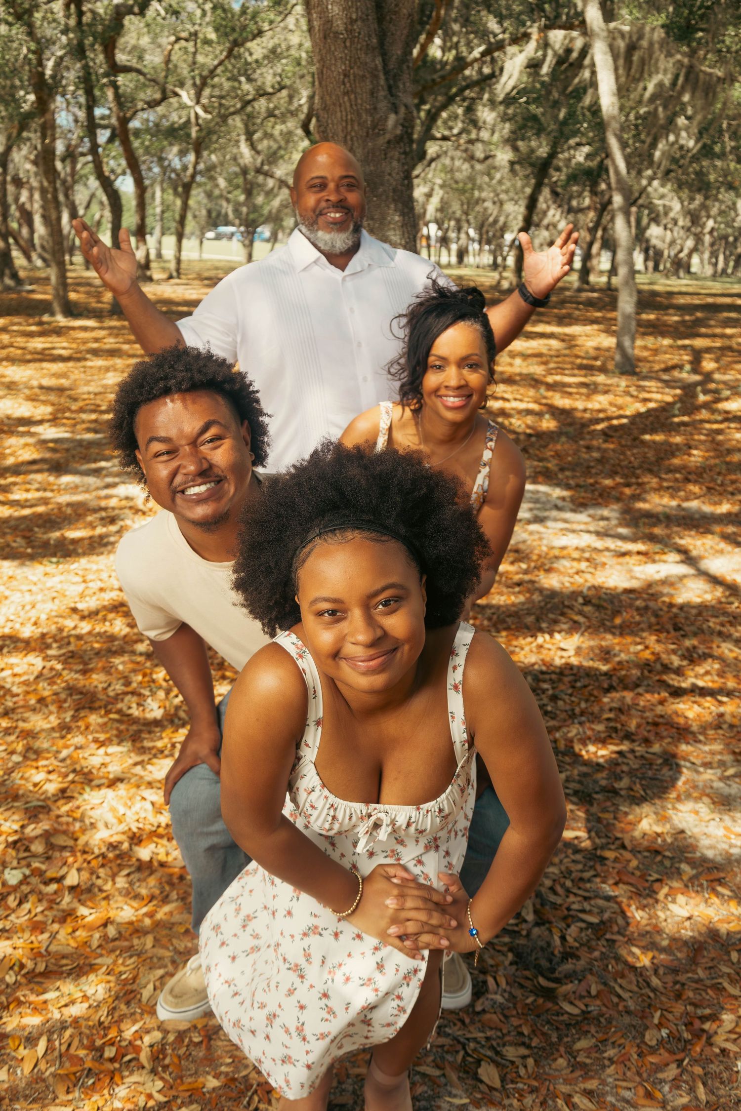 Joyful family of four posing playfully among autumn leaves in a wooded park.