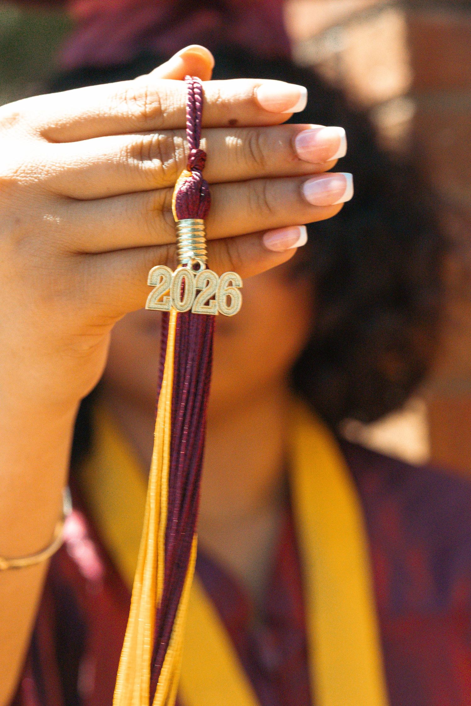 Close-up of graduate holding maroon and gold tassel with 2026 charm in front of blurred background.