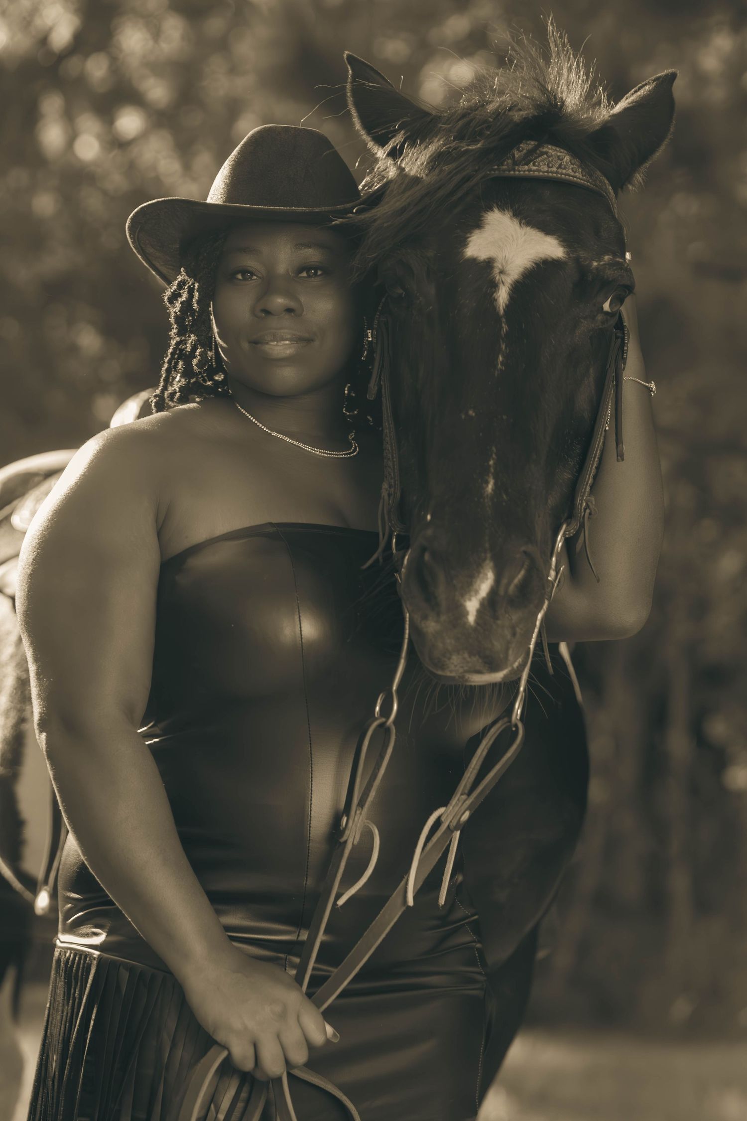 Sepia toned portrait of woman in black leather corset and cowboy hat standing beside dark horse.