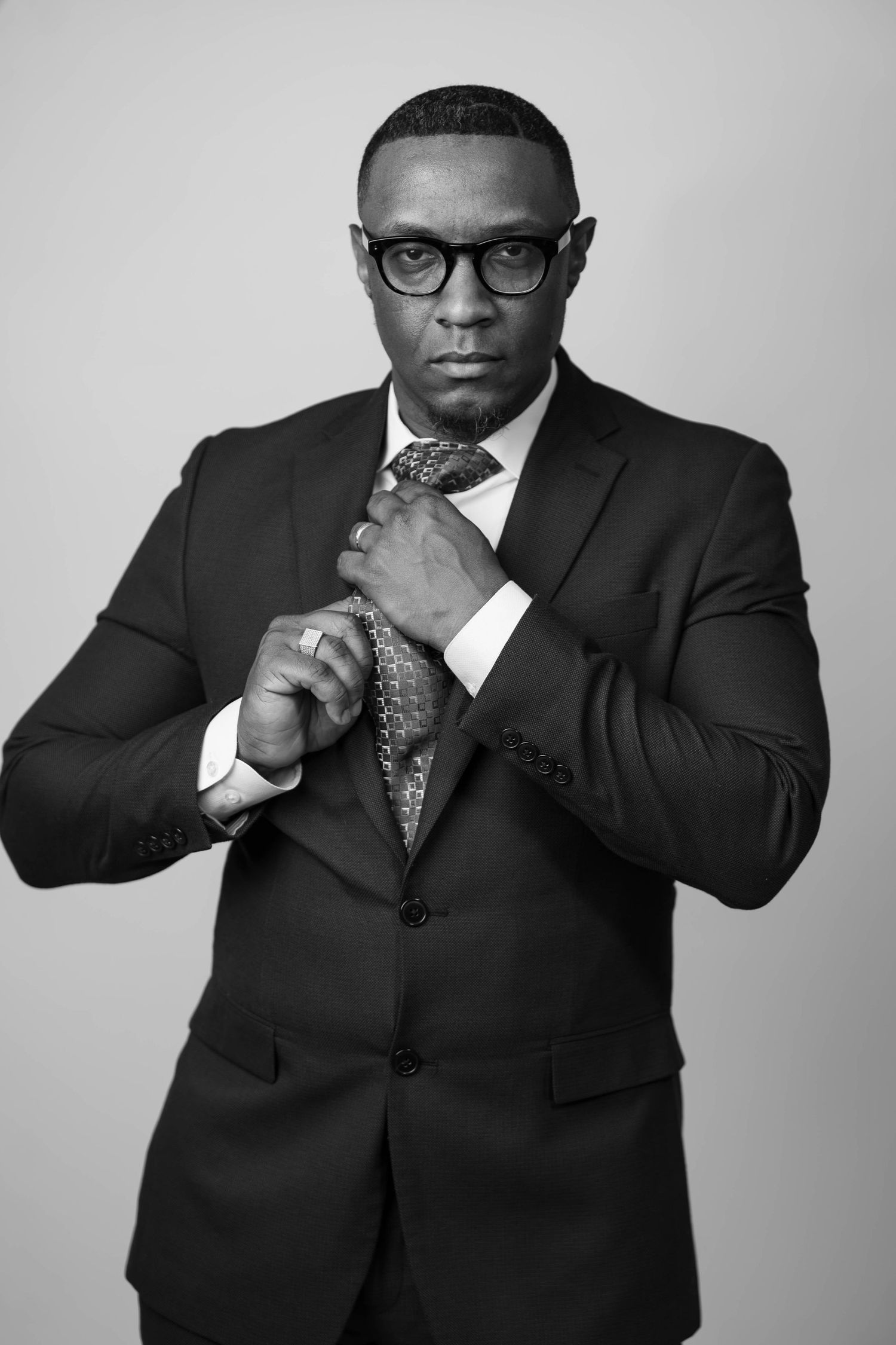 Black and white portrait of confident man in suit adjusting tie wearing glasses.