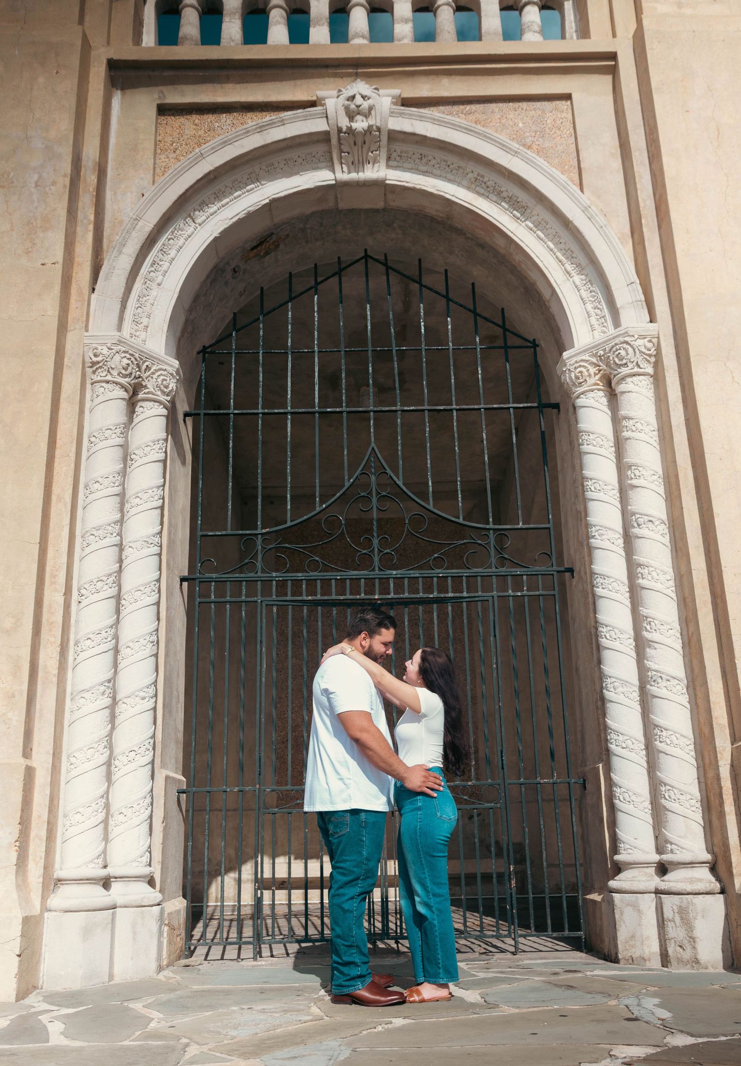 Couple sharing a romantic moment kissing under an ornate stone archway gate.