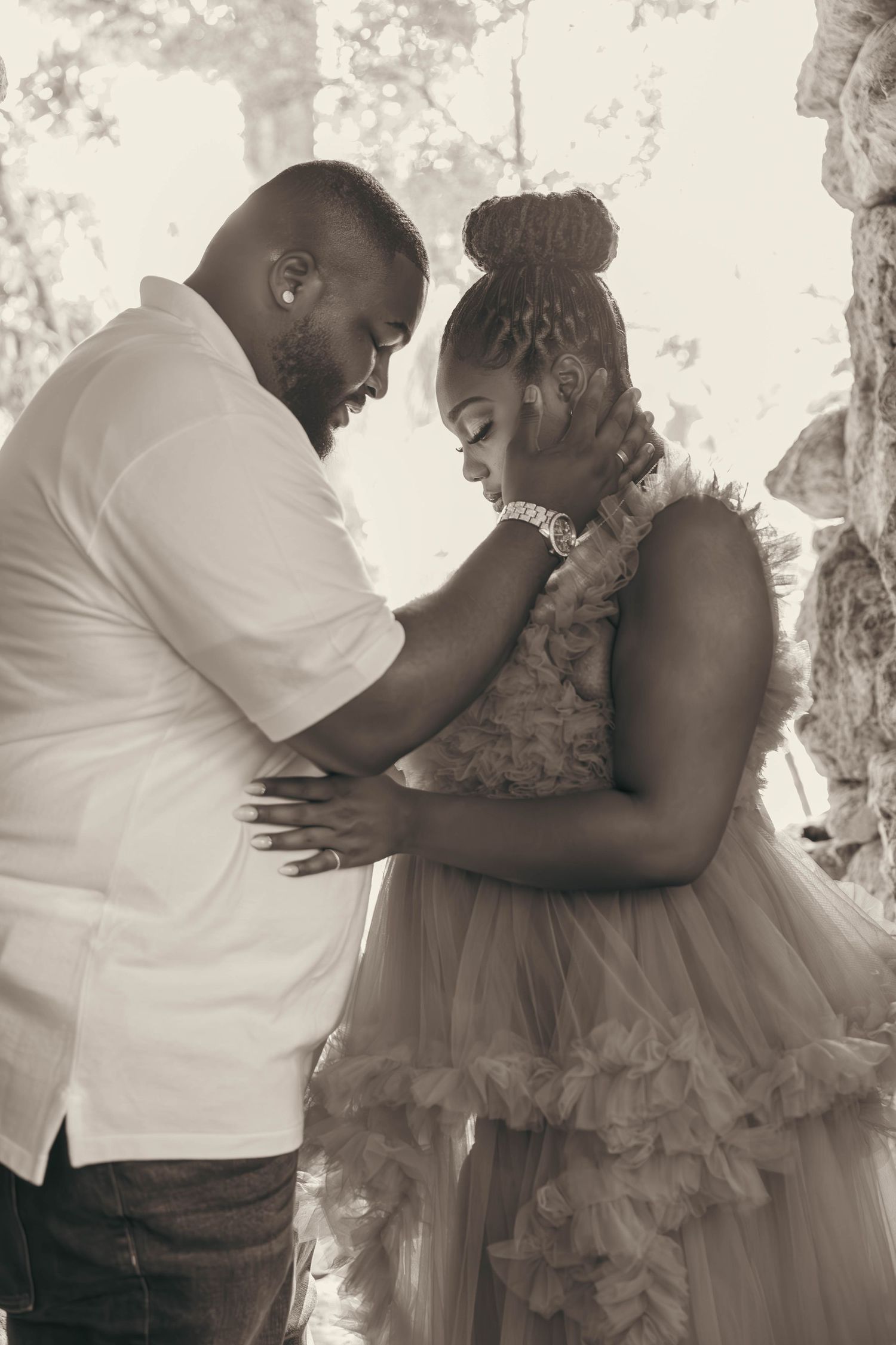 Black couple sharing intimate moment in black and white maternity photo under soft natural light.