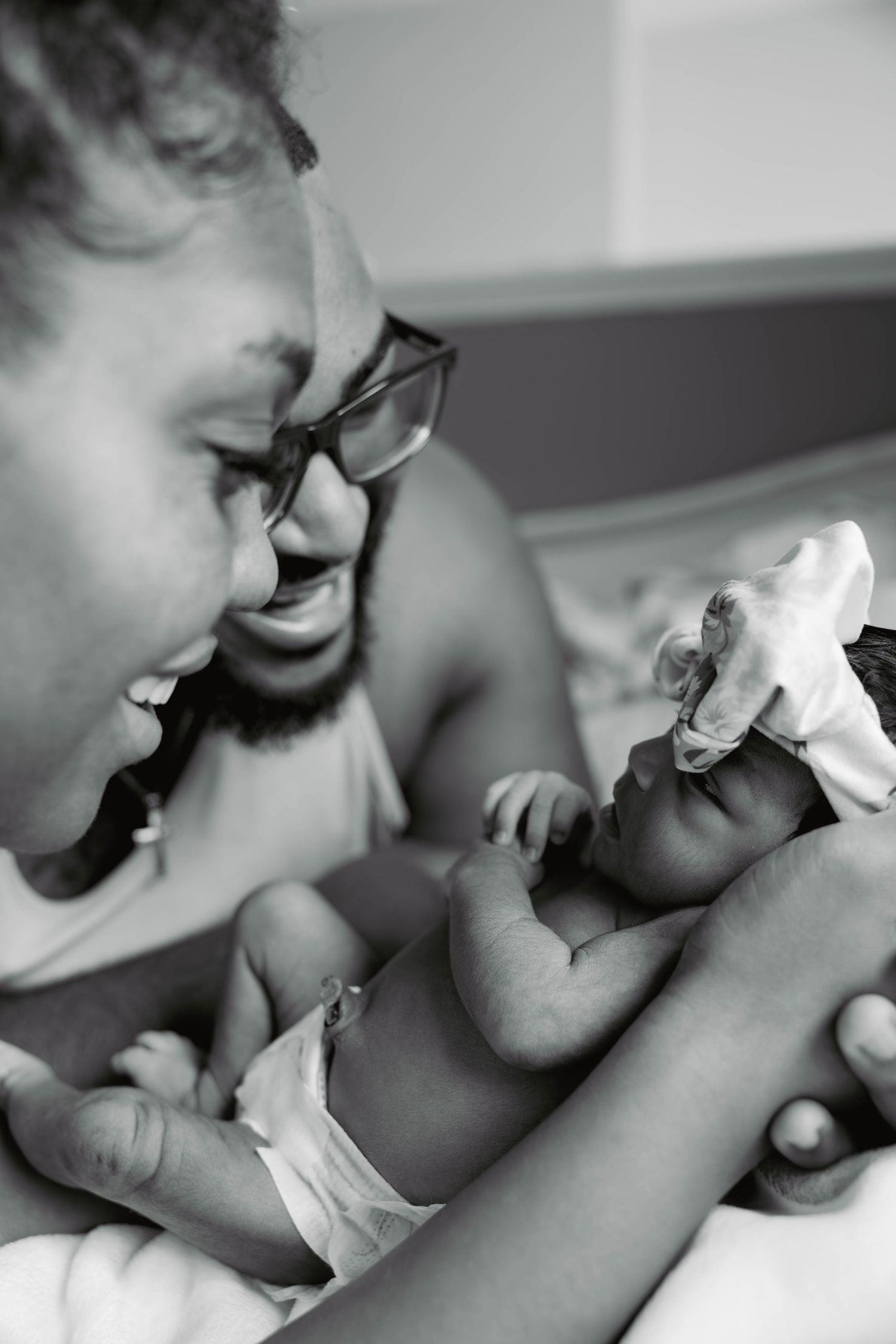 Black and white photo of joyful father holding newborn baby in hospital room.