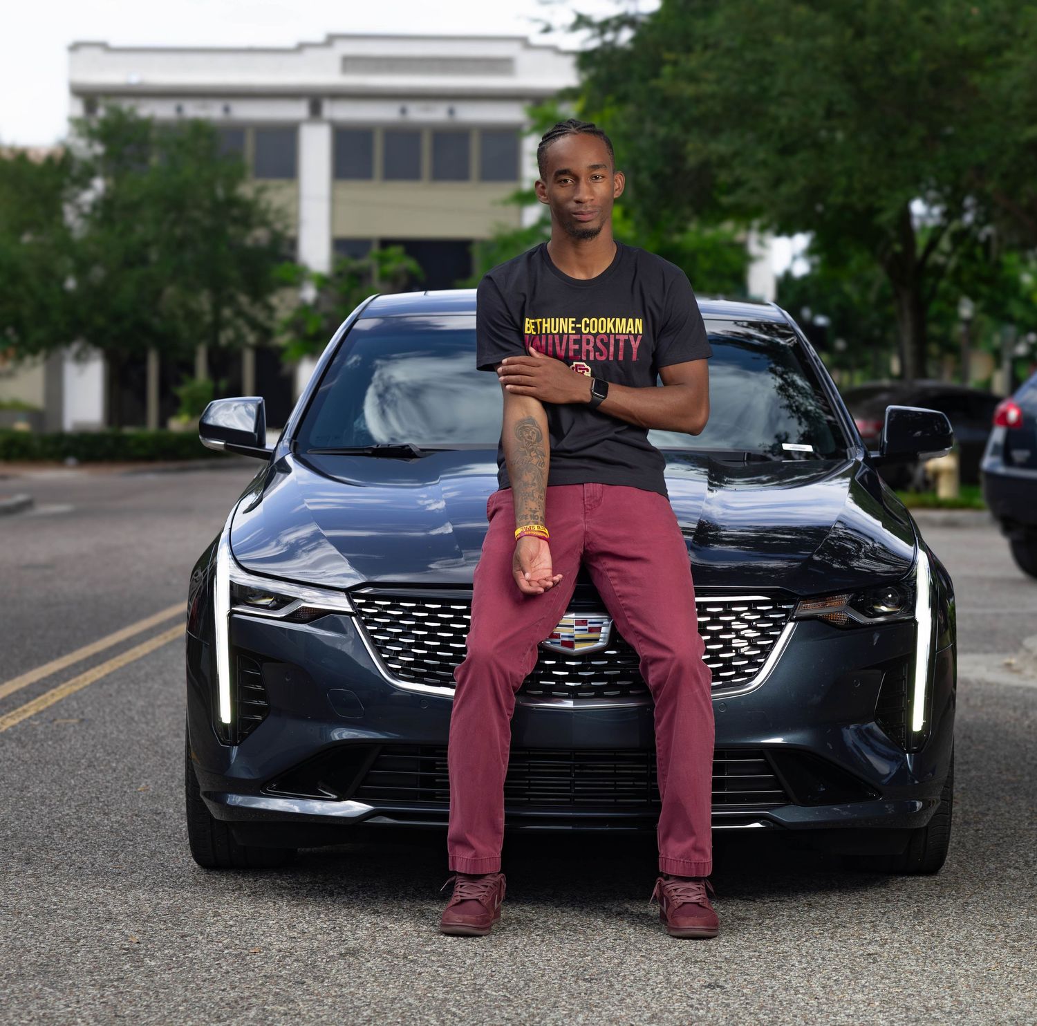 Young man in Bethune-Cookman University shirt leaning confidently against a dark luxury SUV outdoors.