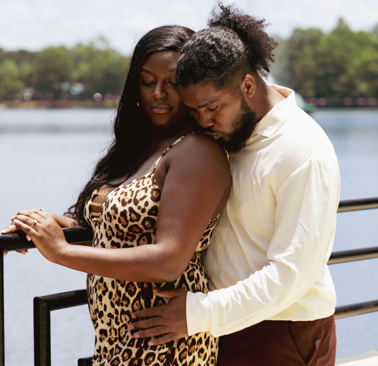 Romantic couple embracing on waterfront deck, woman in leopard print dress leaning on railing.