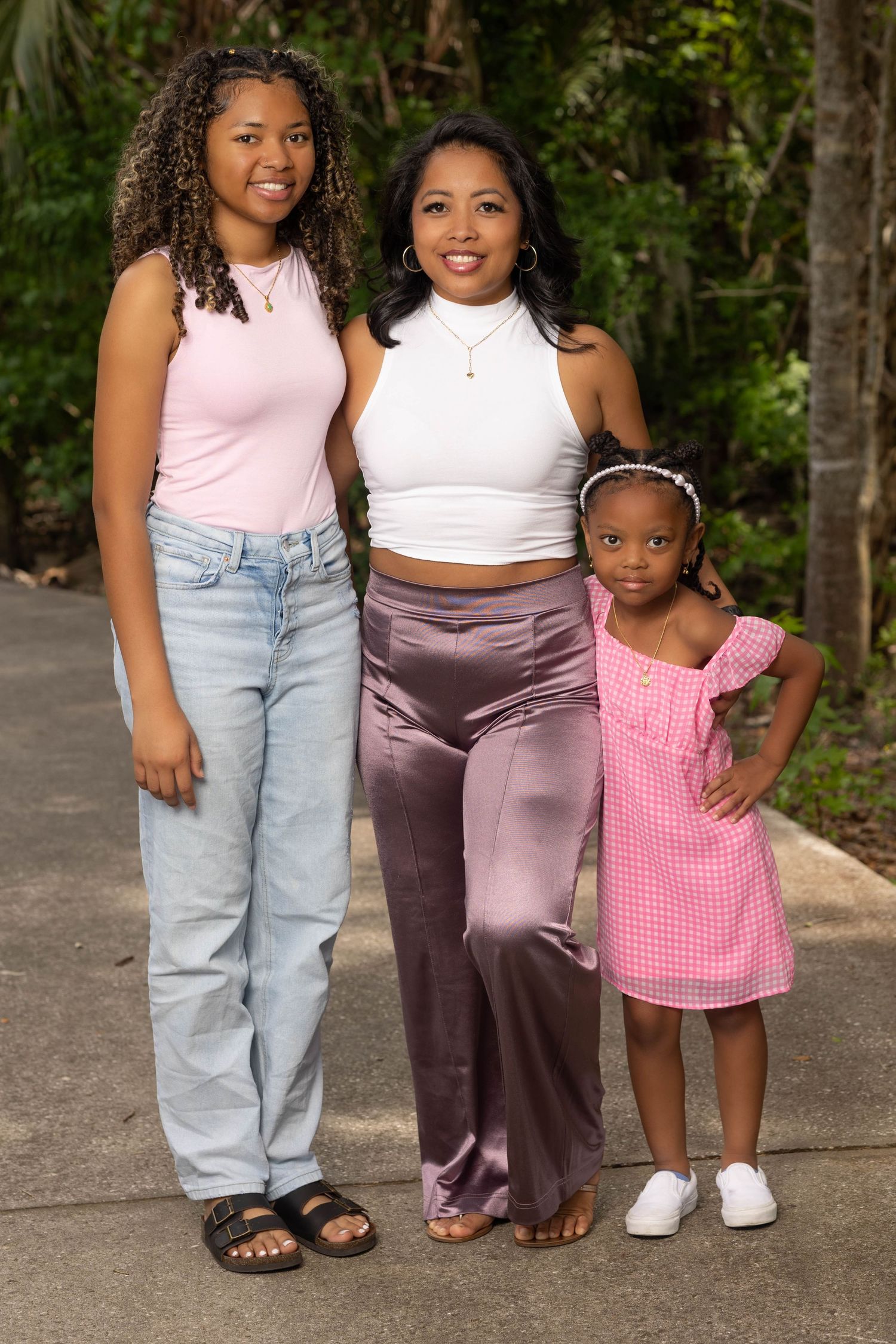 Three generations of women posing together outdoors surrounded by lush green trees.
