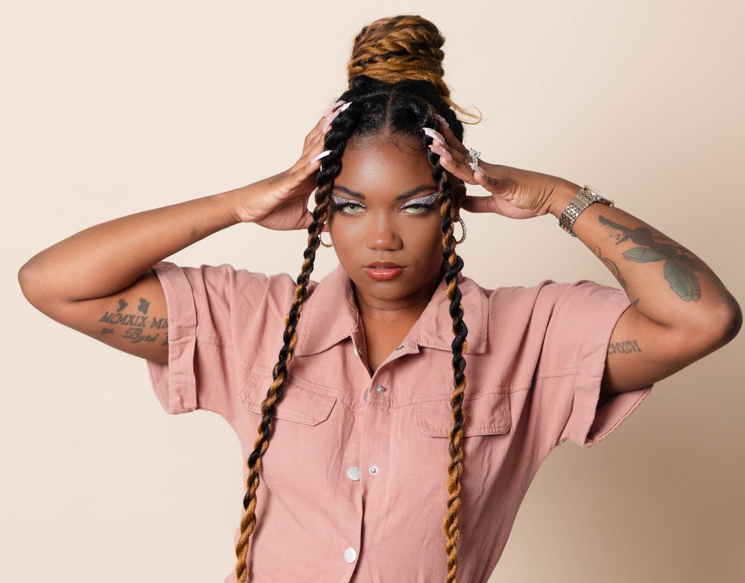 Woman with colorful twisted braids in pink shirt holding her hair up.