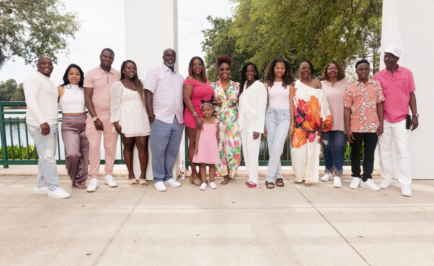 Large Black family group photo outdoors, dressed in coordinating pink and white outfits, smiling together.