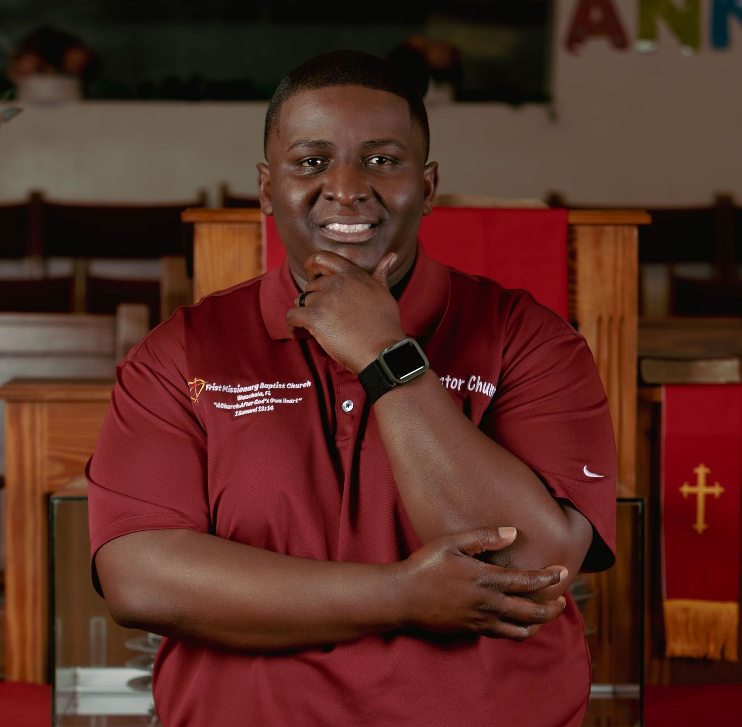 Smiling man in red polo shirt poses confidently in a church setting with wooden pews in the background.