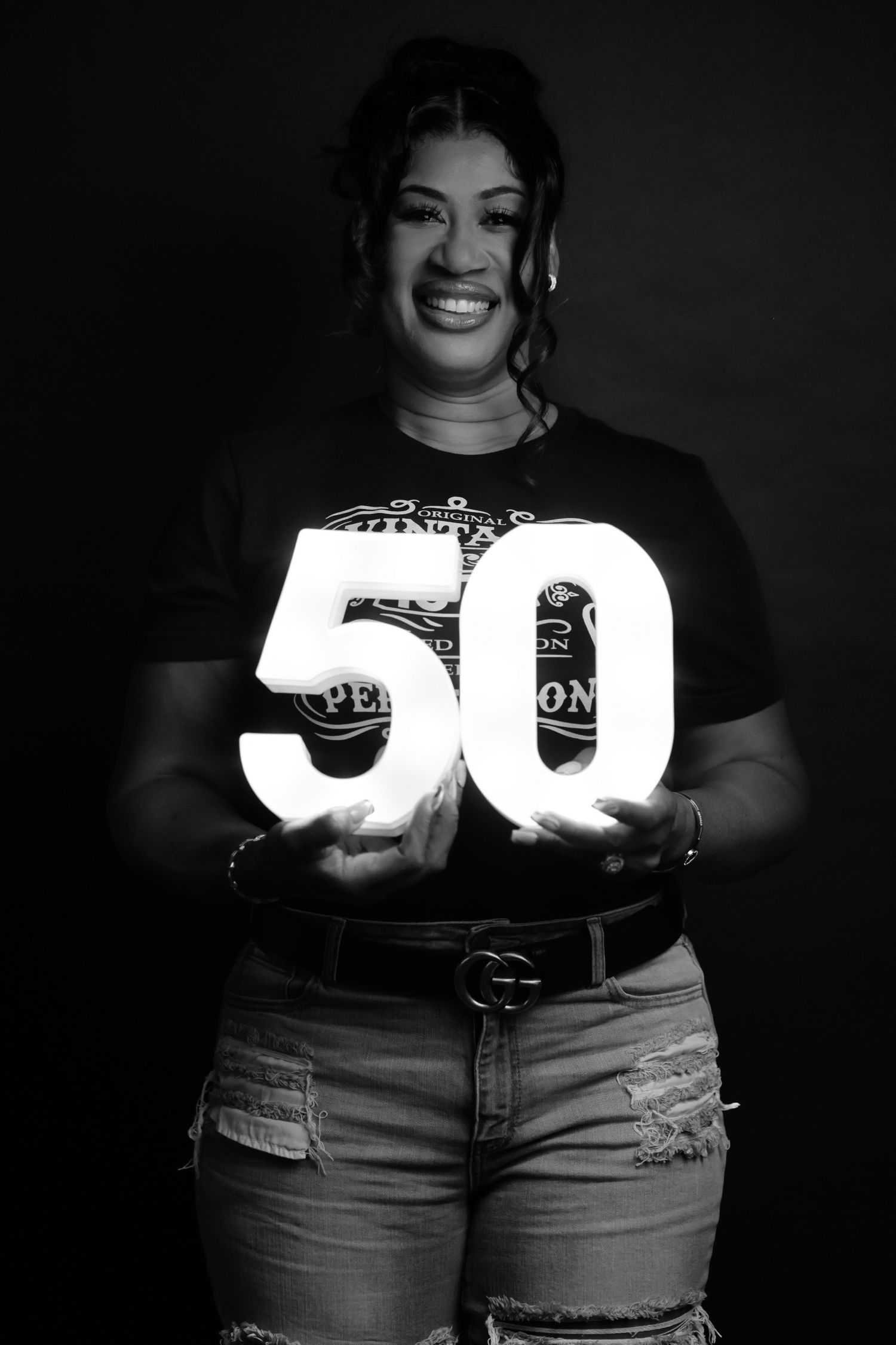Black and white photo of smiling woman holding illuminated number 50 sign for milestone birthday.