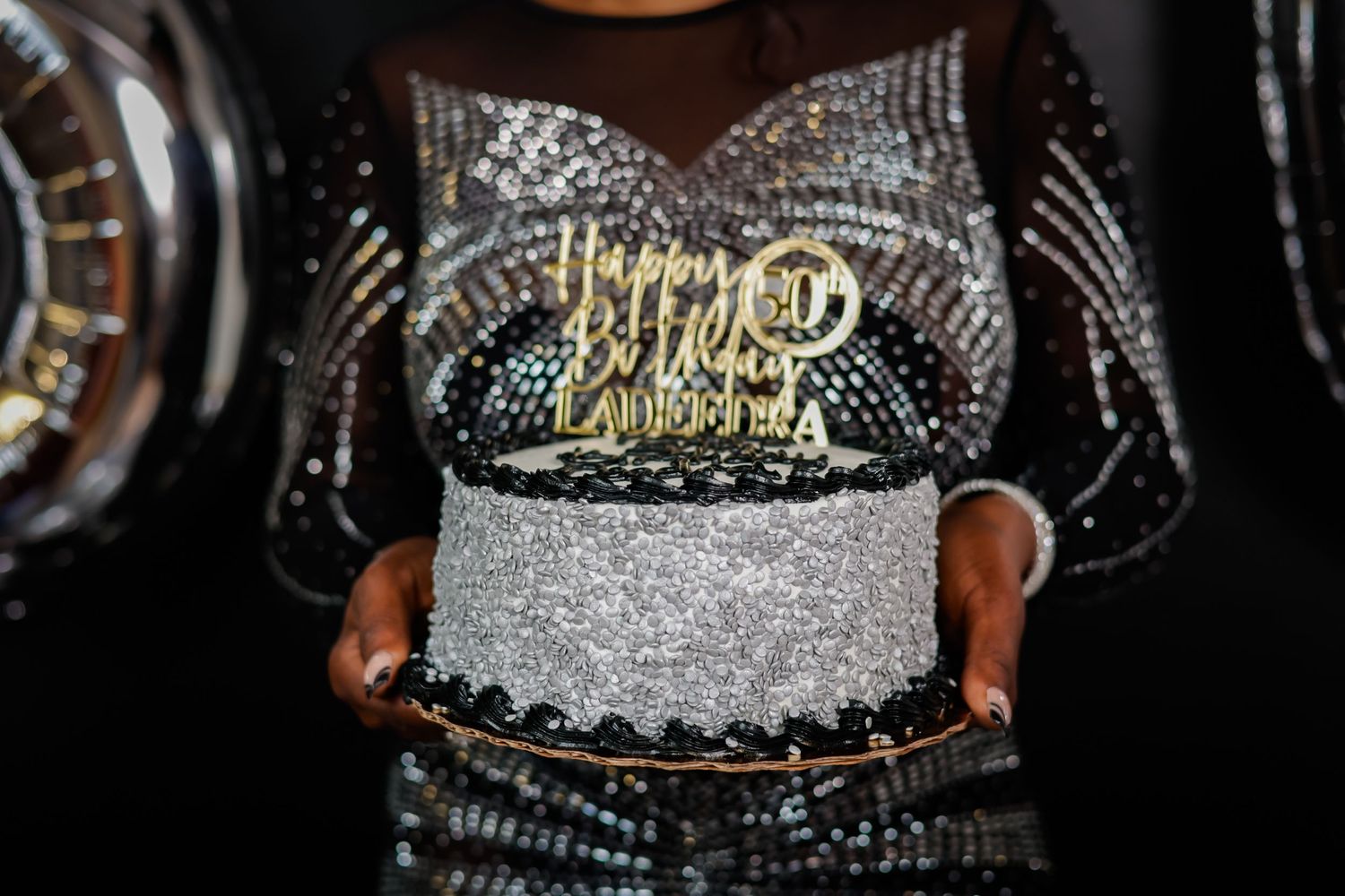 Hands holding a glittery silver birthday cake with a gold Happy Birthday topper.