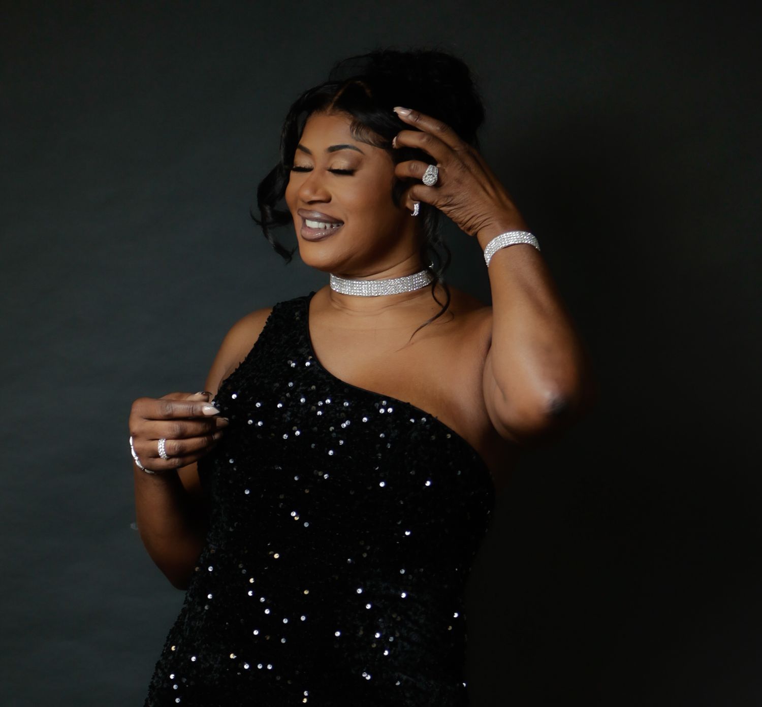 A woman in a black sequin dress poses confidently with jewelry and a choker necklace.