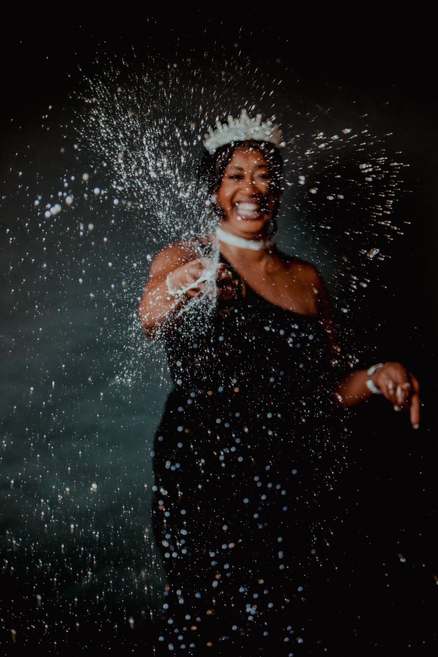 A joyful woman in a crown celebrates with confetti and water splashing around her.